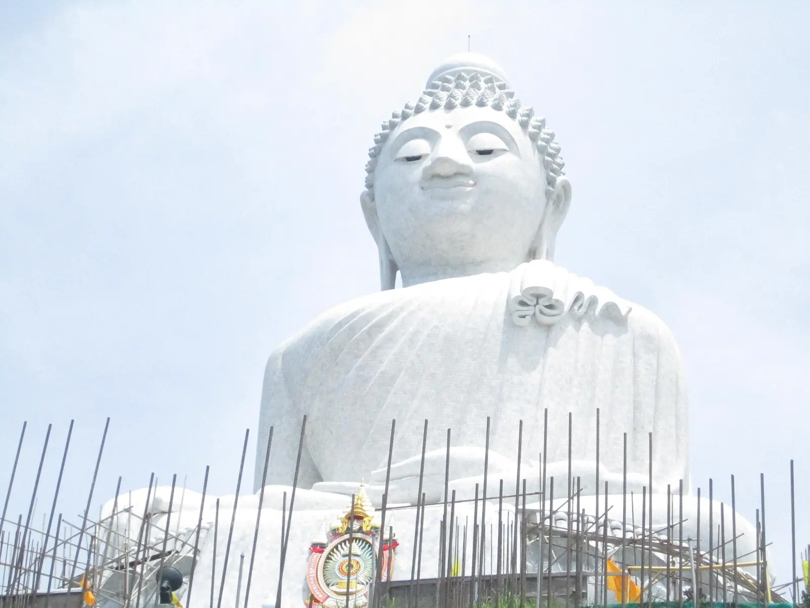 Close view of the head and shoulders of the white marble Big Buddha of Phuket against a pale sky