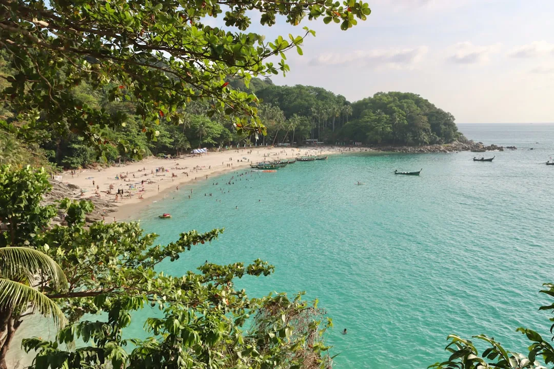 Panoramic view of Phuket coastline with longtail boats, green hills, and turquoise water